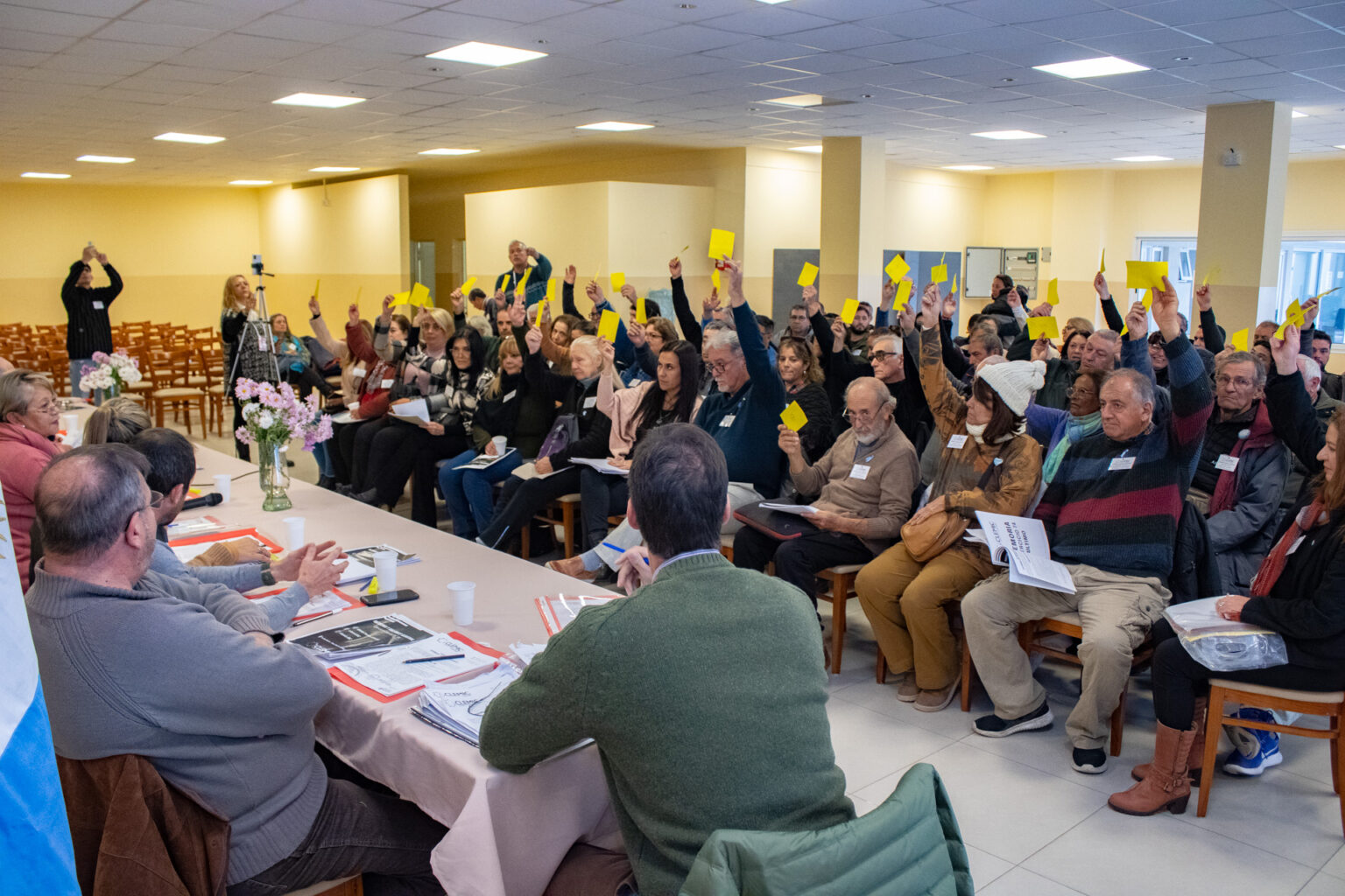 Personas levantando la mano con una tarjeta amarilla para votar en la Asamblea General Ordinaria