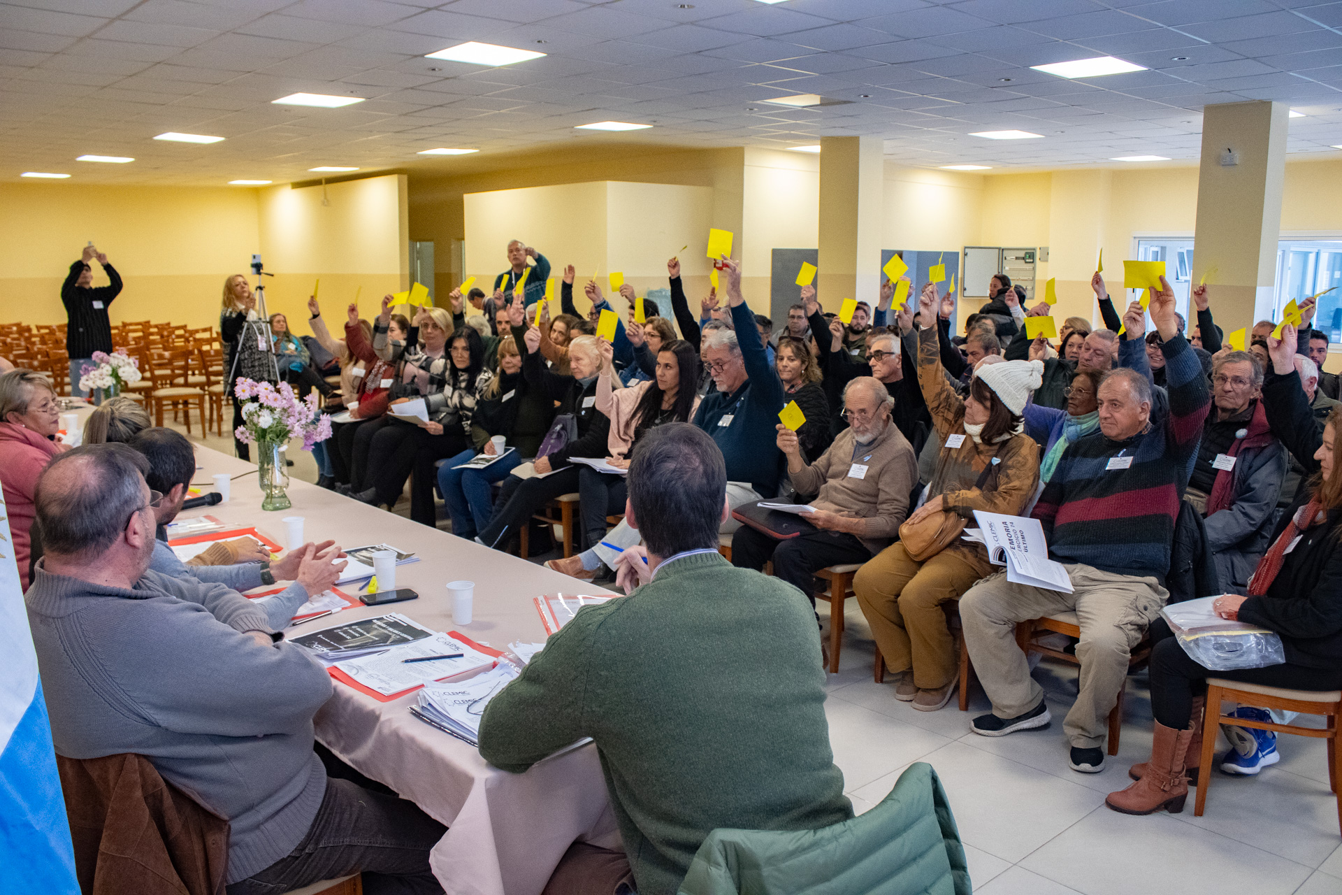 Personas levantando la mano con una tarjeta amarilla para votar en la Asamblea General Ordinaria